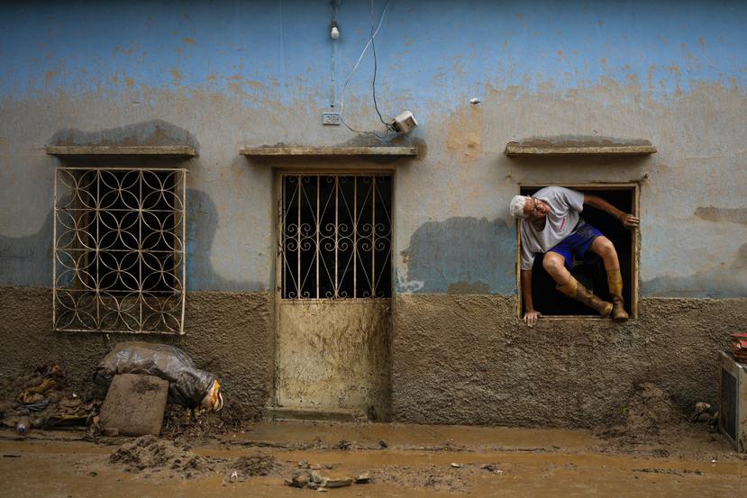 José Medina sale por la ventana de casa inundada por el desborde de un riachuelo a causa de las fuertes lluvias.