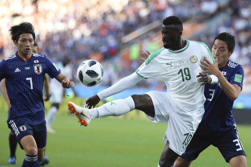 Mbaye Niang, de Senegal, busca manejar el balón contra Gaku Shibasaki y Gen Shoji. (AP)