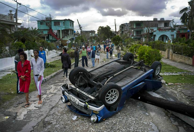 Ciudadanos cubanos caminan junto a un automóvil que fue volcado por los fuertes vientos del tornado que azotó a La Habana. (AP / Ramón Espinosa)