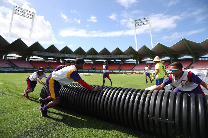 Estudiantes de la Puerto Rico Baseball Academy ensayan la colocación de la lona sobre el terreno del estadio  como parte de los preparativos.
