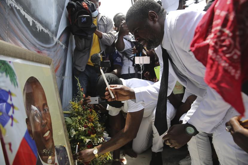 Jimmy "Barbecue" Cherizier, un expolicía que dirige una coalición de bandas criminales llamada "G9", enciende una vela  frente a un retrato del presidente asesinado Jovenel Moïse durante una manifestación el lunes 26 de julio de 2021 para exigir justicia, en Puerto Príncipe, Haití.