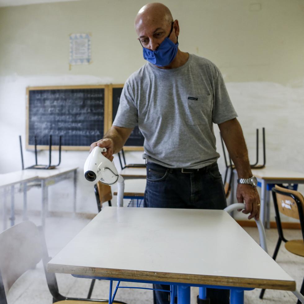 A man disinfects desks in a classroom so as to prevent the spread of COVID-19, at the Melissa Bassi school in Rome, Monday, Aug. 31, 2020. Despite a spike in coronavirus infections, authorities in Europe are determined to send children back to school. They want to narrow learning gaps between haves and have-nots that deepened during virus lockdowns – and to get their parents back to work. (Cecilia Fabiano/LaPresse via AP)