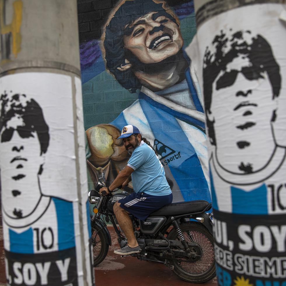 Un fan se prepara para salir en su motocicleta junto a un mural que representa al fallecido astro del fútbol Diego Maradona afuera del club "Estrella de Fiorito", su primer club, en el barrio Fiorito de Buenos Aires, Argentina.