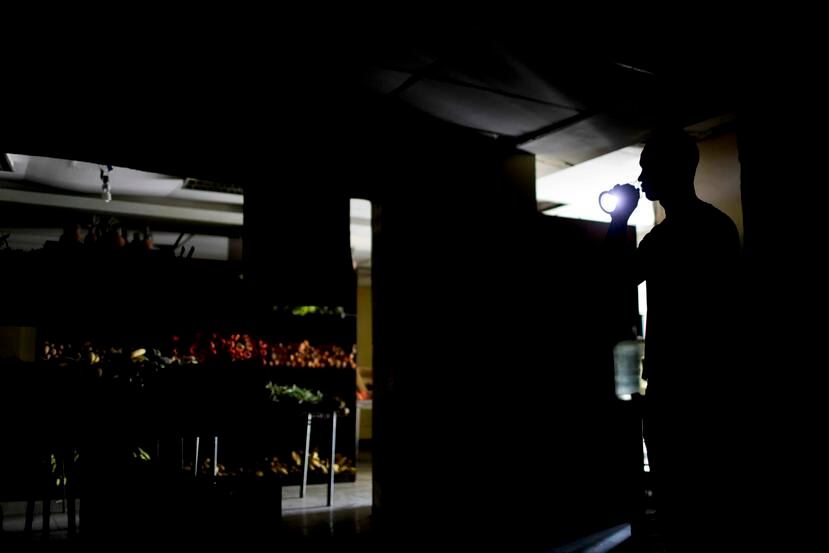 Un hombre alumbra una hilera de un supermercado en Venezuela con una linterna debido a los apagones que agobian al país desde la semana pasada. (AP / Natacha Pisarenko)