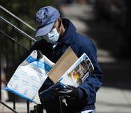 Un empleado del Servicio Postal de Estados Unidos hace una entrega con guantes y mascarilla en Filadelfia, el jueves 2 de abril de 2020. (AP / Matt Rourke)