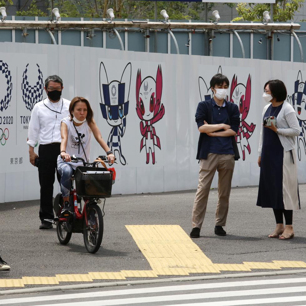 Personas se detienen en un esquina junto a un poster de promoción de los Juegos Olímpicos en Tokio el lunes.