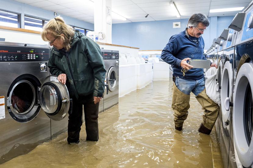 Pamela y Patrick Cerruti sacan monedas de la lavandería Pajaro Coin Laundry en medio de una inundación, el martes 14 de marzo de 2023, en la comunidad de Pajaro, condado Monterey, California.