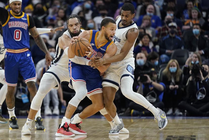 Stephen Curry, en el medio, es defendido por el alero de los Memphis Grizzlies, Dillon Brooks, en el centro a la izquierda, De'Anthony Melton durante la segunda mitad de un juego de baloncesto de la NBA en San Francisco, el jueves 23 de diciembre de 2021.