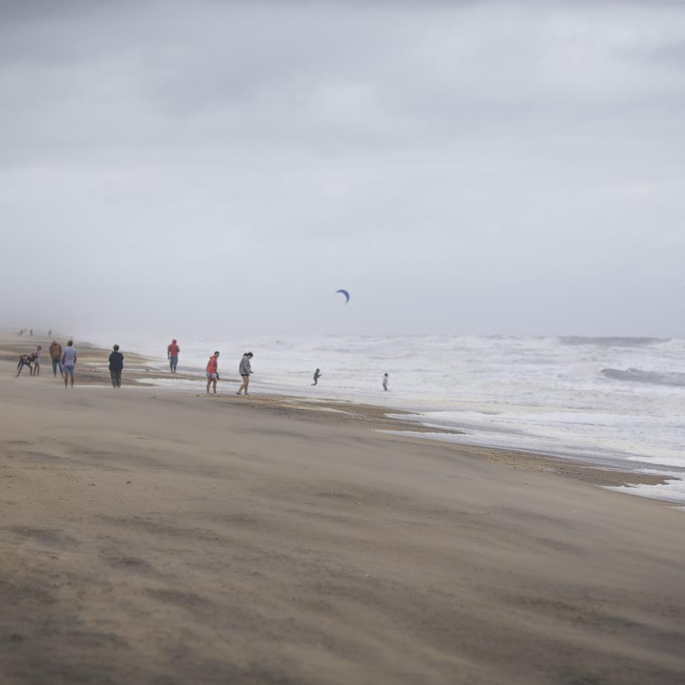 Un grupo de bañistas mira a gente haciendo kitesurf entre las olas provocadas por la tormenta tropical Ophelia, el sábado 23 de septiembre de 2023 en Virginia Beach, Virginia. (AP Foto/John C. Clark)