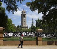 Dos hombres caminan frente a un letrero de protesta que fue colocado en los portones de la  UPR en Río Piedras durante el proceso huelgario que impulsaron los universitarios el pasado año. (GFR Media)
