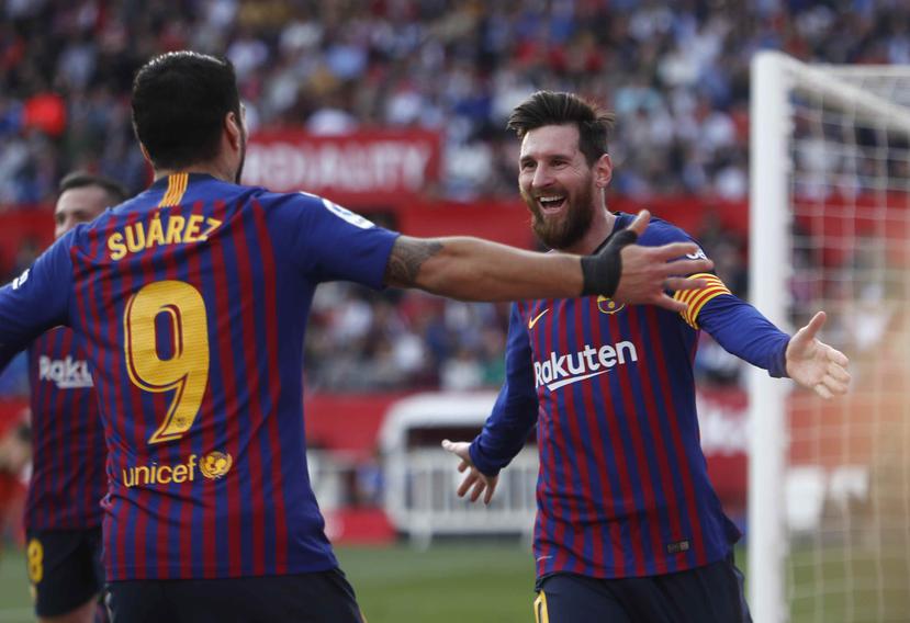 Lionel Messi festeja con su compañero Luis Suárez tras anotar su tercer gol en el partido de la Liga española, en Sevilla. (AP)