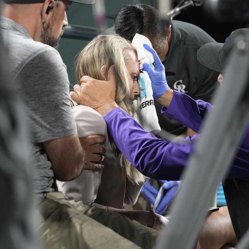 Kelsey Wingert, reportera de televisión de los Rockies de Colorado, recibe atención luego de que una pelota bateada de foul la golpeó en la frente, durante el juego del lunes 16 de mayo de 2022, en Denver