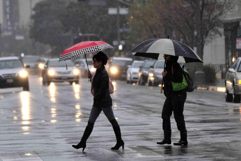 Dos mujeres se cubren con sombrillas de la lluvia, mientras caminan por una carretera. (GFR Media)