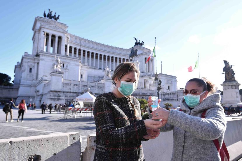 Dos mujeres con mascarillas comparten desinfectante de manos frente a uno de los edificios emblemáticos de Roma. (AP)