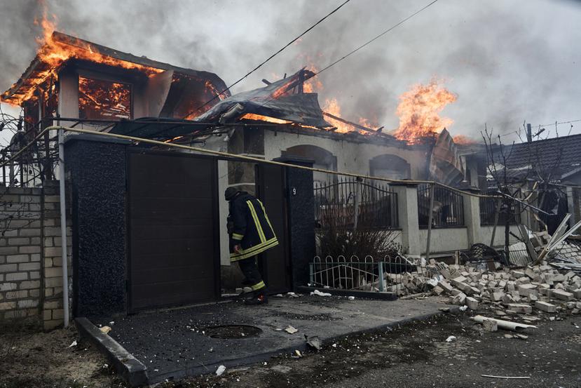 Un bombero se para en una casa en llamas golpeada por los bombardeos rusos en Kherson, Ucrania, en la víspera de Navidad ortodoxa el viernes 6 de enero de 2023.
