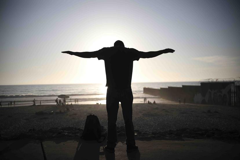 Un hombre se estira cerca del muro fronterizo que separa a México de Estados Unidos en una playa de Tijuana, México. (AP)