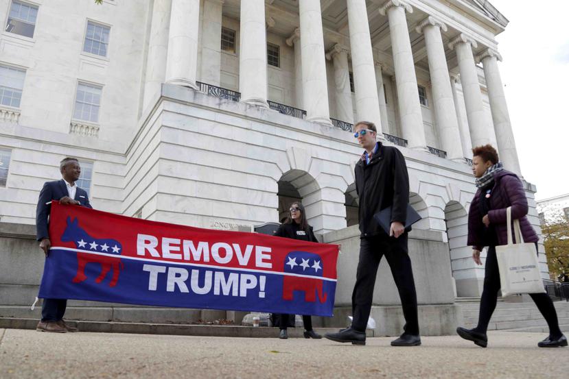 Un par de manifestantes sostienen una pancarta en la que exigen la salida del presidente Donald Trump, en el exterior del edificio en que la exembajadora de Estados Unidos para Ucrania, Marie Yovanovitch. (AP/Julio Cortez)