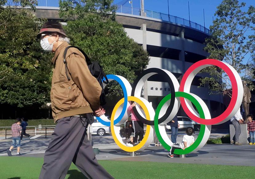 Un hombre protegido por una máscara para evitar posibles contagios da la espalda a unos aros olímpicos instalados en Tokio. (EFE)