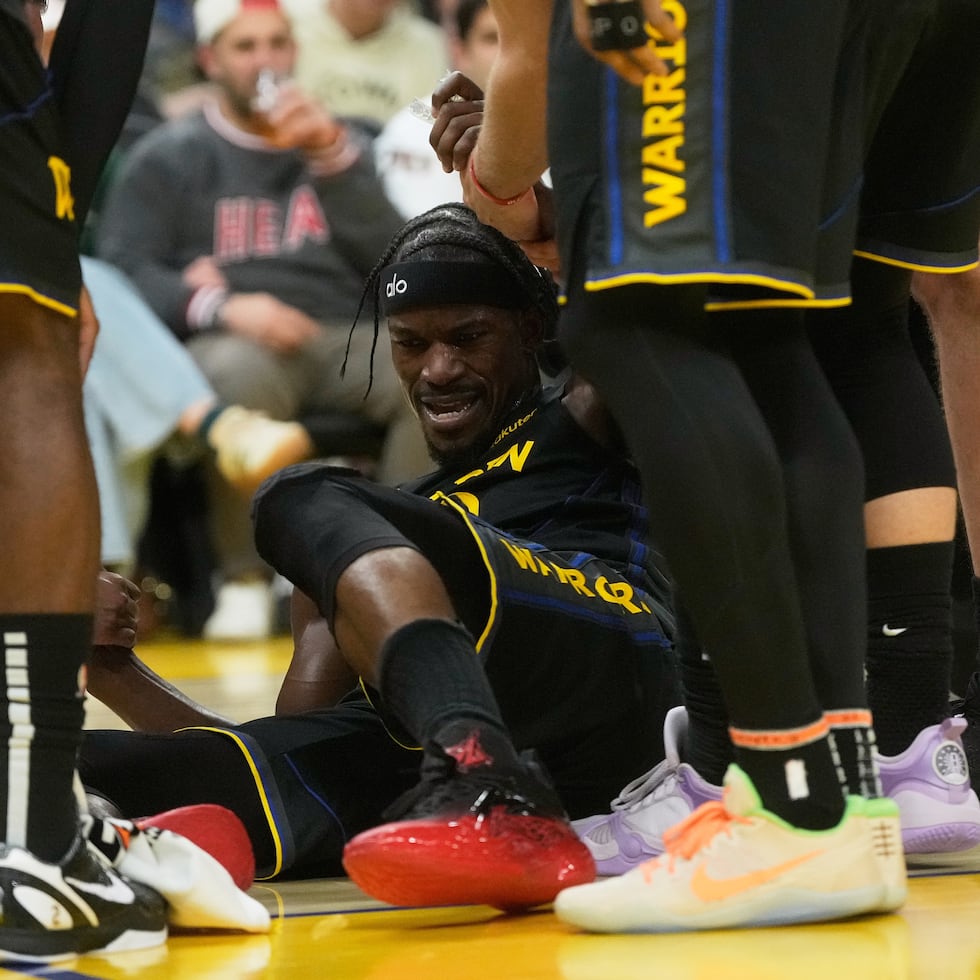 Jimmy Butler, de los Warriors de Golden State, es auxiliado para levantarse por sus compañeros de equipo, luego de lesionarse la rodilla derecha ante Miami.