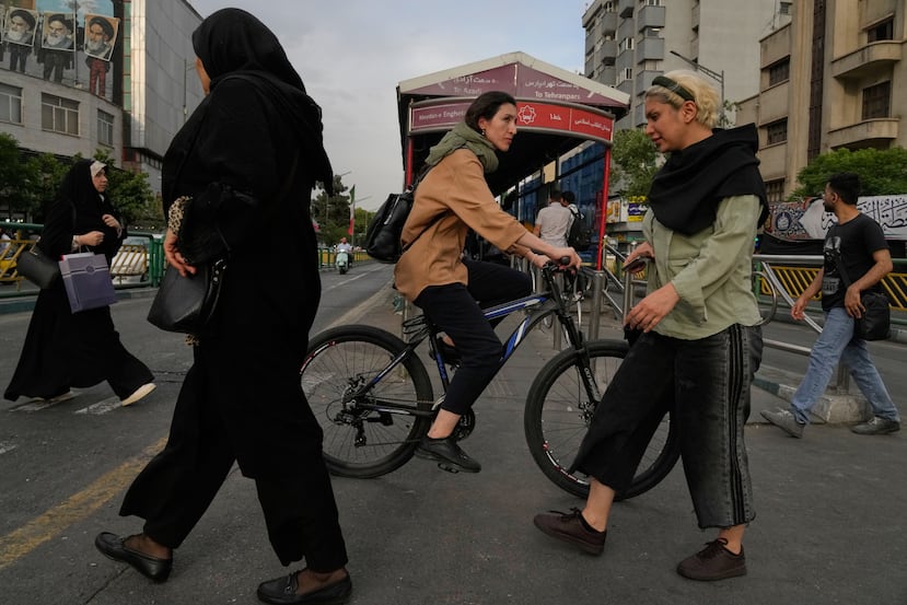 Una mujer monta en bicicleta mientras otras personas cruzan una calle en el centro de Teherán, Irán, el domingo 24 de mayo de 2026. (Foto AP/Vahid Salemi)