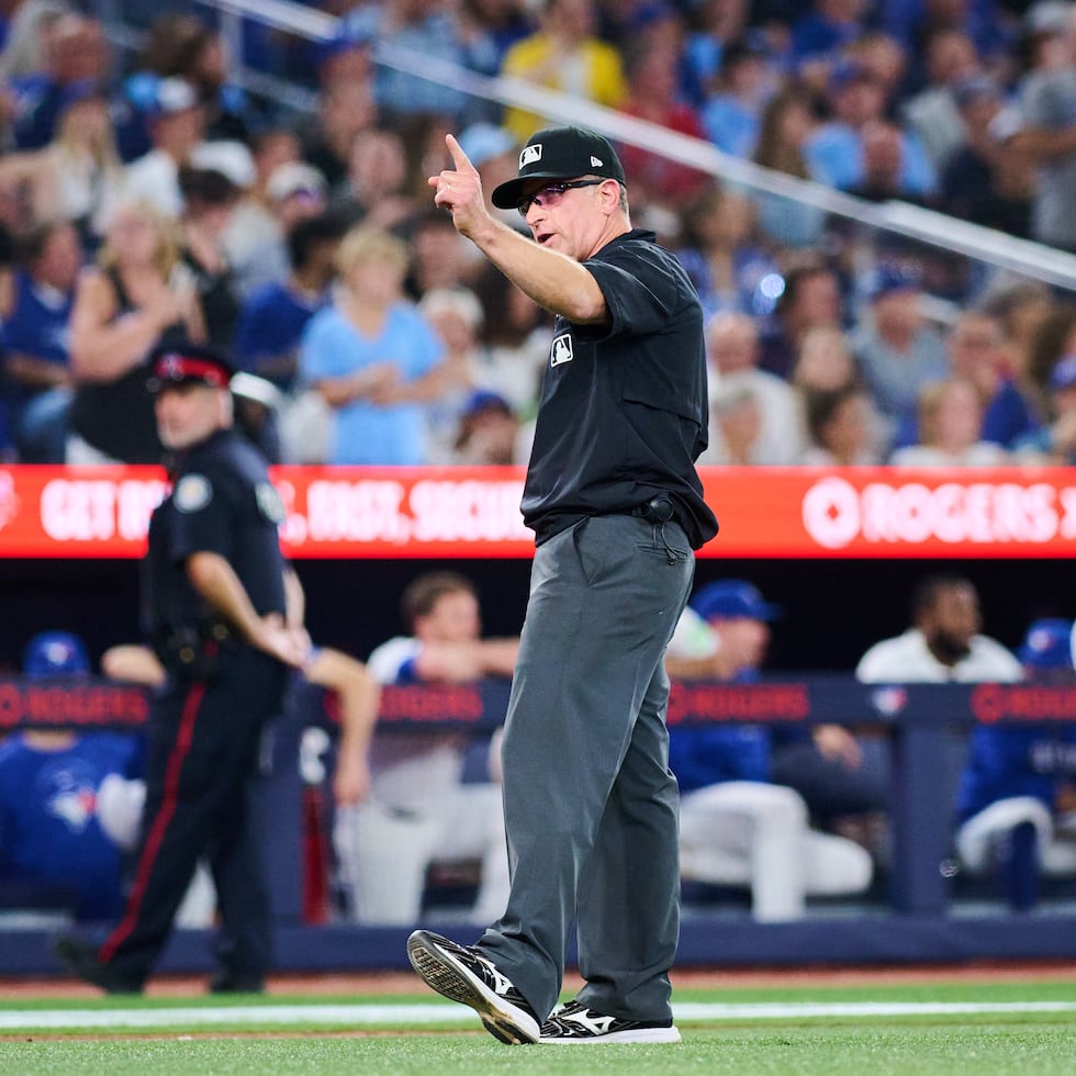 El árbitro Chris Guccione, al centro, anuncia una revisión de la controversial jugada durante la séptima entrada del partido entre los Blue Jays de Toronto y los Red Sox de Boston.