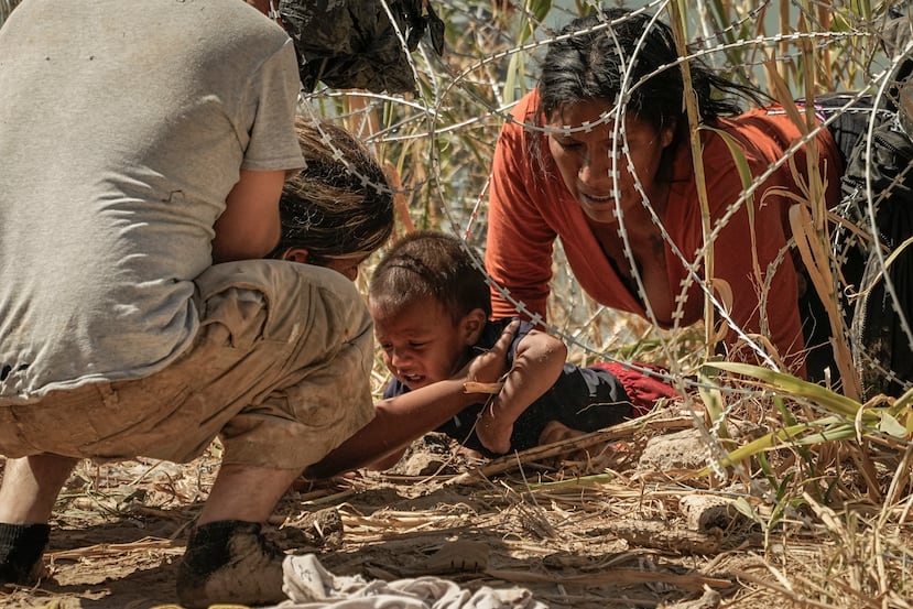 Migrantes que cruzaron hacia Estados Unidos desde México pasan bajo alambre de púas a las orillas del río Bravo (Grande), el jueves 21 de septiembre de 2023, en Eagle Pass, Texas.
