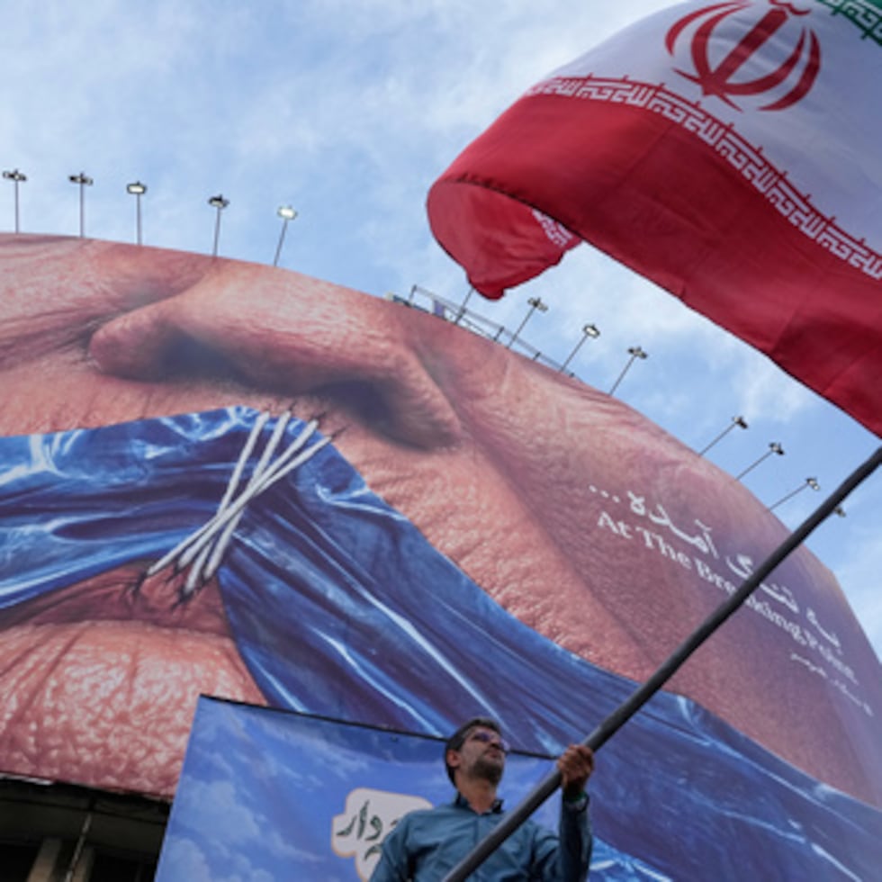 Un hombre ondea una bandera iraní para una campaña progubernamental bajo un cartel que muestra el estrecho de Ormuz y los labios del presidente de Estados Unidos, Donald Trump, cosidos, en una plaza en el centro de Teherán, Irán.