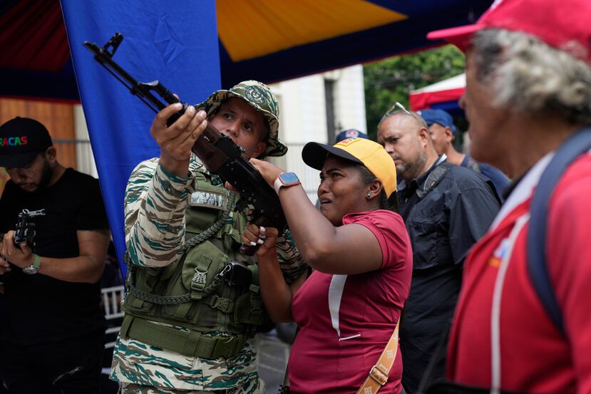 Un miembro de la Milicia Nacional Bolivariana le muestra a una mujer cómo operar un arma durante ejercicios militares en Caracas, Venezuela, el sábado 20 de septiembre de 2025. (Foto AP/Ariana Cubillos)