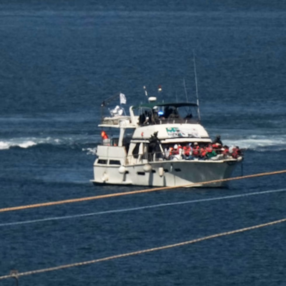 Activistas con chalecos salvavidas color anaranjado a bordo de un barco de la Flotilla Sumud con destino a Gaza mientras soldados de la Armada de Israel lo escoltan a puerto, el 2 de octubre de 2025, en Ashdod, Israel, después de interceptar a la embarcación mientras se acercaba a la costa de Gaza.