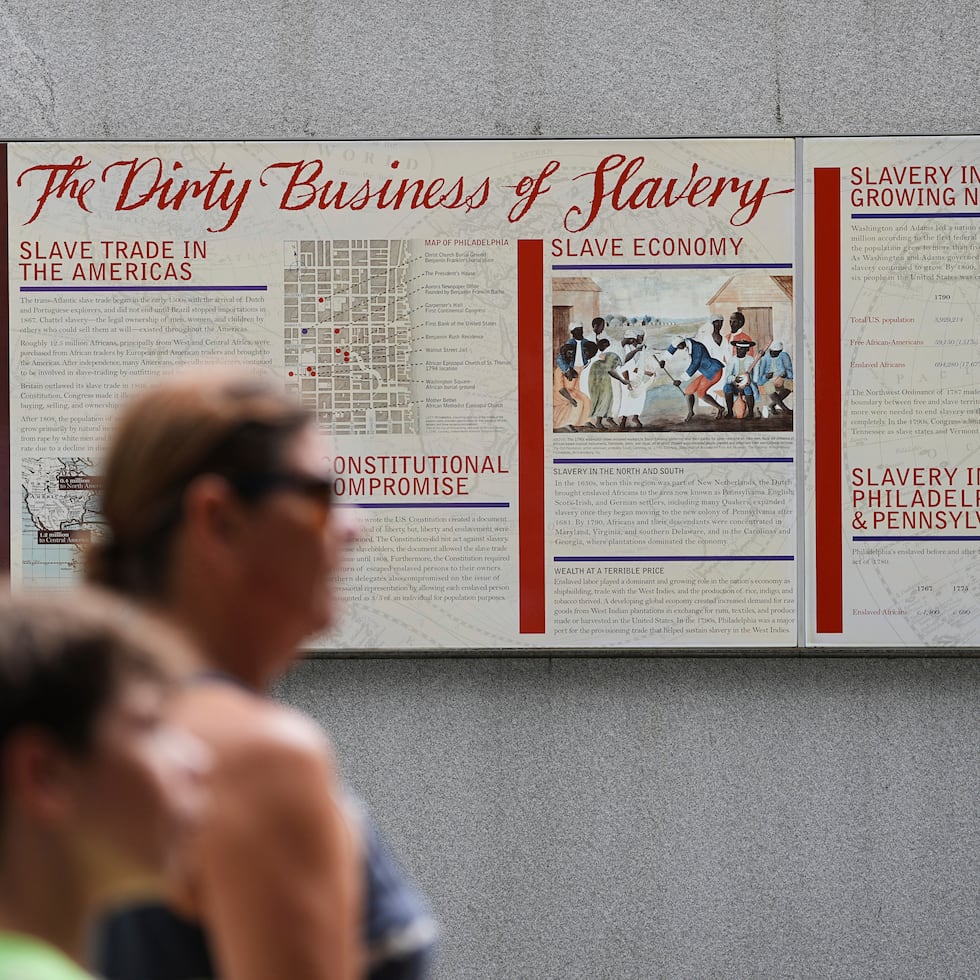 Varias personas pasan frente a un panel informativo en el Sitio de la Casa del Presidente, en Filadelfia.