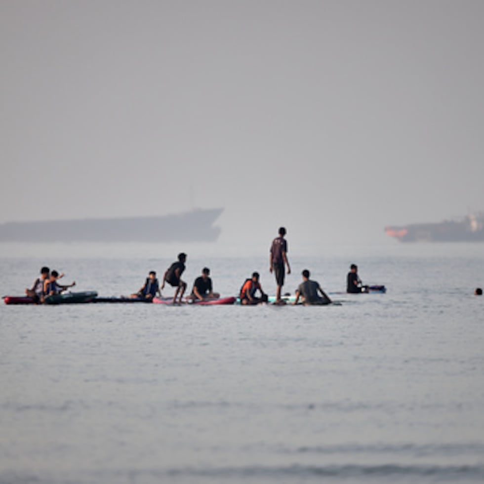 Personas se reúnen en tablas de remo en aguas poco profundas mientras buques de carga y de servicio están anclados en el Estrecho de Ormuz en Irán.