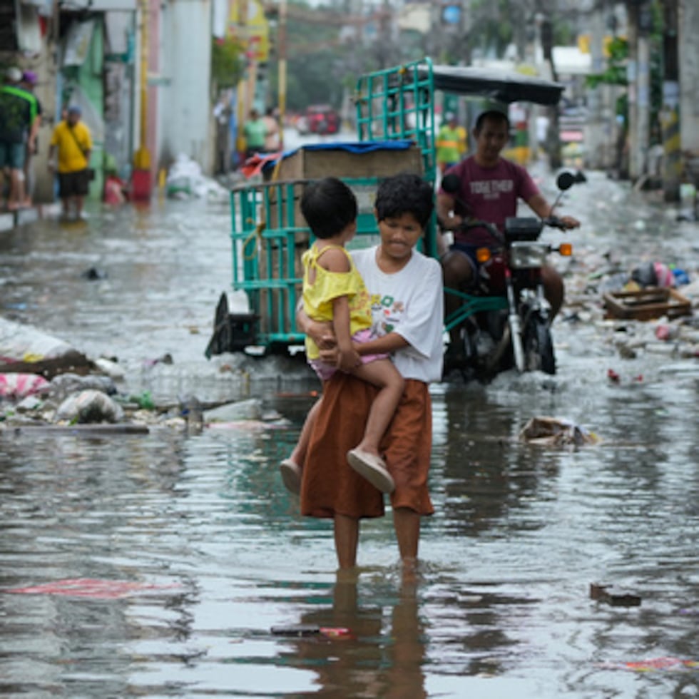 A woman and child crosses a flooded street due to Typhoon Fung-wong and high tide on Monday, Nov. 10, 2025, in Navotas, Philippines. (AP Photo/Aaron Favila)