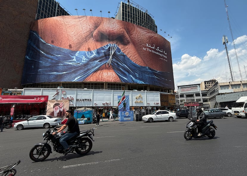 Vehículos circulan junto a una valla publicitaria con una imagen del estrecho de Ormuz y los labios cosidos del presidente estadounidense Donald Trump, en una plaza del centro de Teherán, Irán, el sábado 2 de mayo de 2026. (Foto AP/Vahid Salemi)