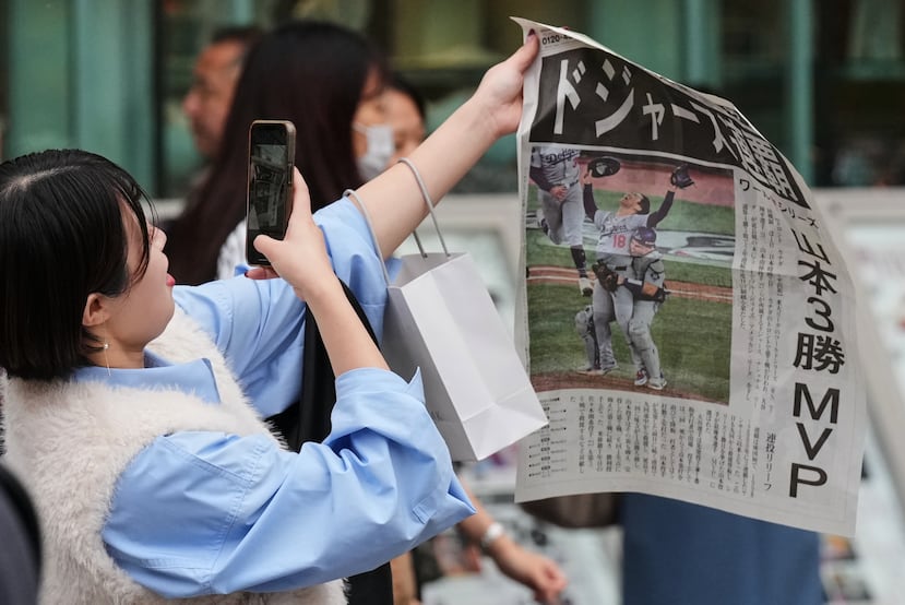 Una mujer en Tokio toma una foto de la edición extra del periódico con la victoria de los Dodgers de Los Ángeles ante los Blue Jays de Toronto en la Serie Mundial.