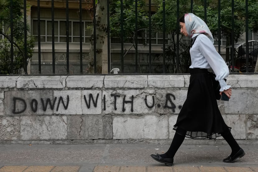 Una mujer pasa junto a un grafiti antiestadounidense pintado en la pared de la Universidad de Teherán, en la calle Enqelab-e-Eslami (Revolución Islámica), en el centro de Teherán, Irán, el sábado 25 de abril de 2026. (Foto AP/Vahid Salemi)