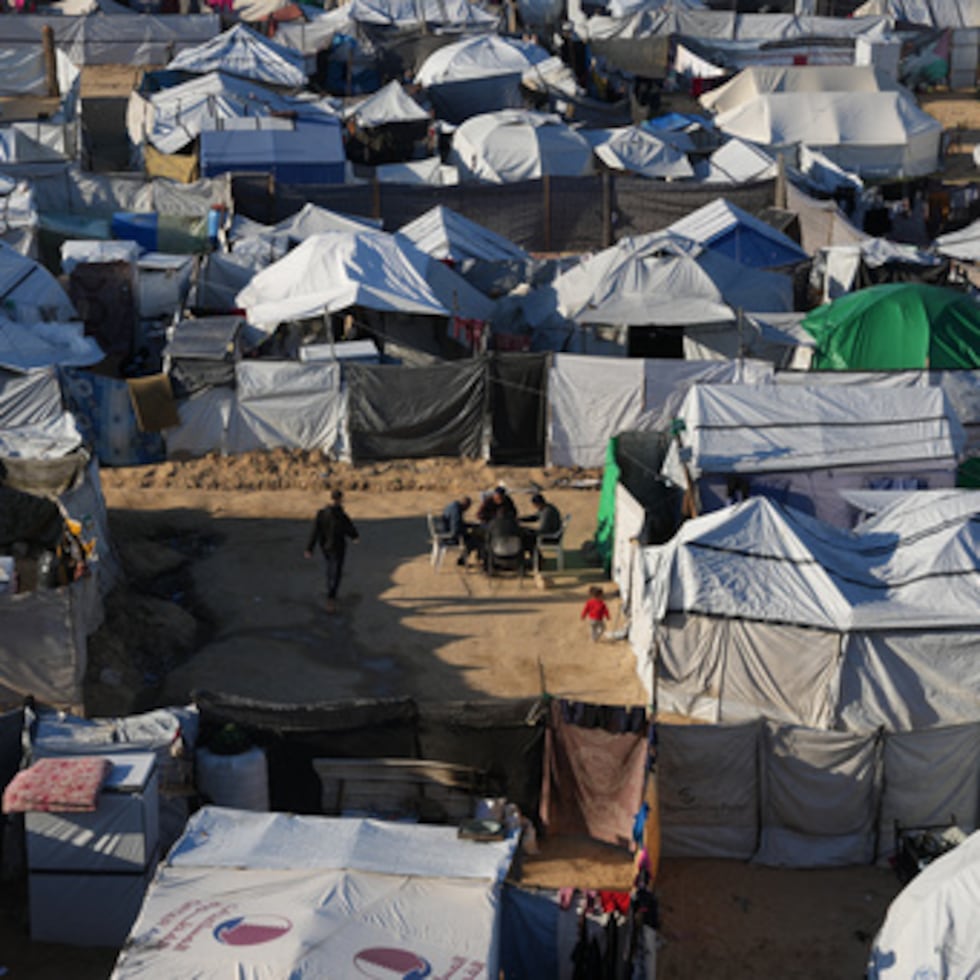 Palestinos desplazados se reúnen frente a una tienda de campaña en un campamento temporal en Deir al-Balah, en el centro de la Franja de Gaza, el sábado 17 de enero.