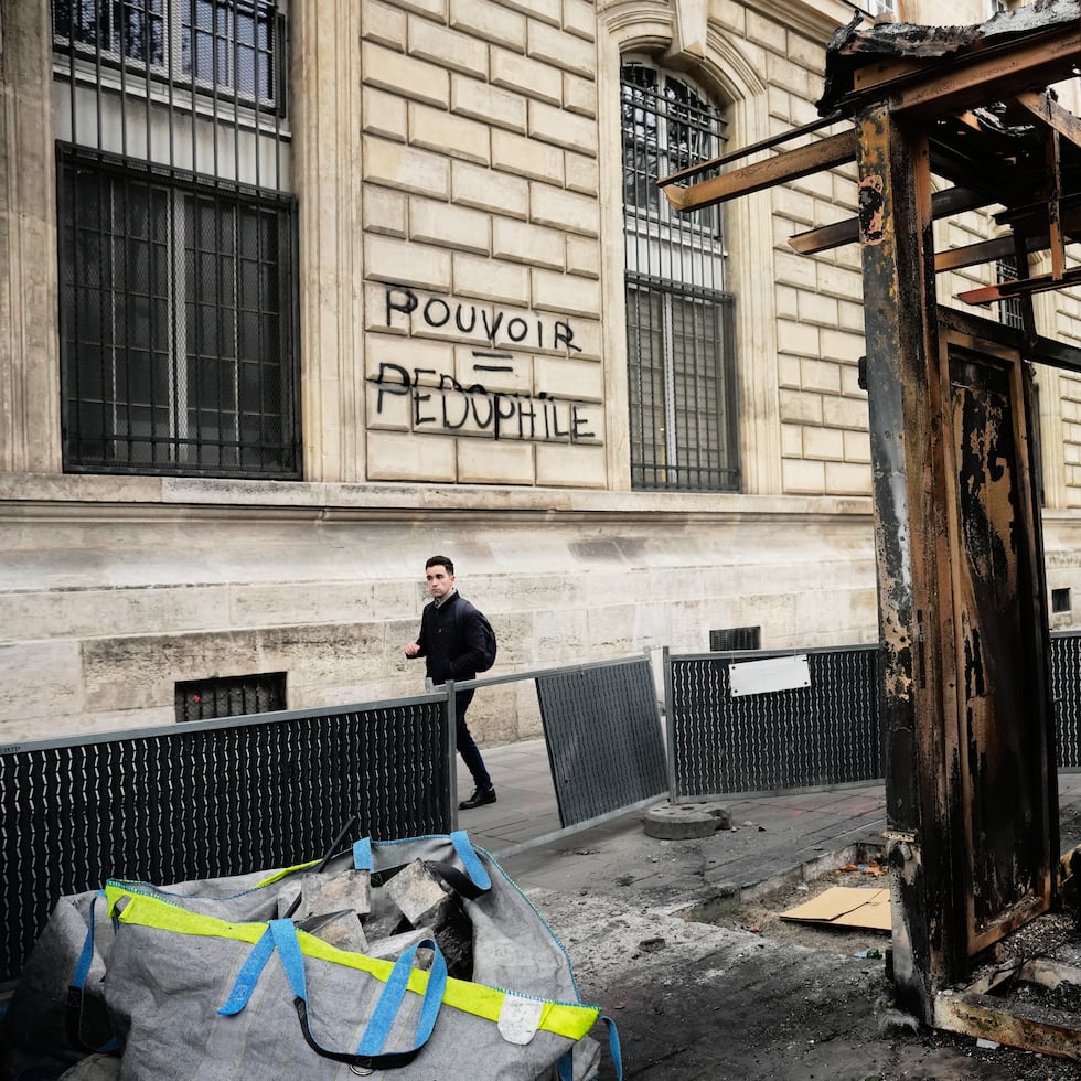 Una mujer camina frente a un edificio en París con grafitis que dicen "Los ultrarricos contra todos" y "Sin justicia no hay paz. Descansa en paz, El Hacen", tras las protestas del fin de semana contra el costo de vida, que derivaron en disturbios y saqueos en distintas partes de Francia.