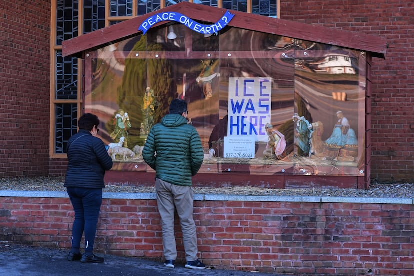 Two visitors look at a nativity display, which features an "ICE WAS HERE" sign in the spot for the baby Jesus, outside St. Susanna Church, Tuesday, Dec. 9, 2025, in Dedham, Mass. (AP Photo/Charles Krupa)
