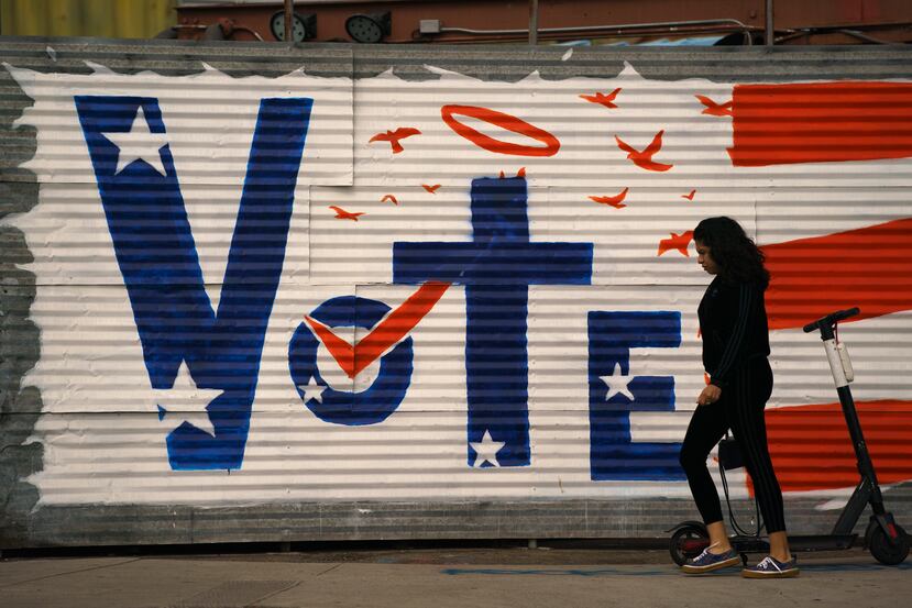 Una mujer camina frente a un letrero de votación pintado en una pared en un área de Venice Beach en Los Ángeles.