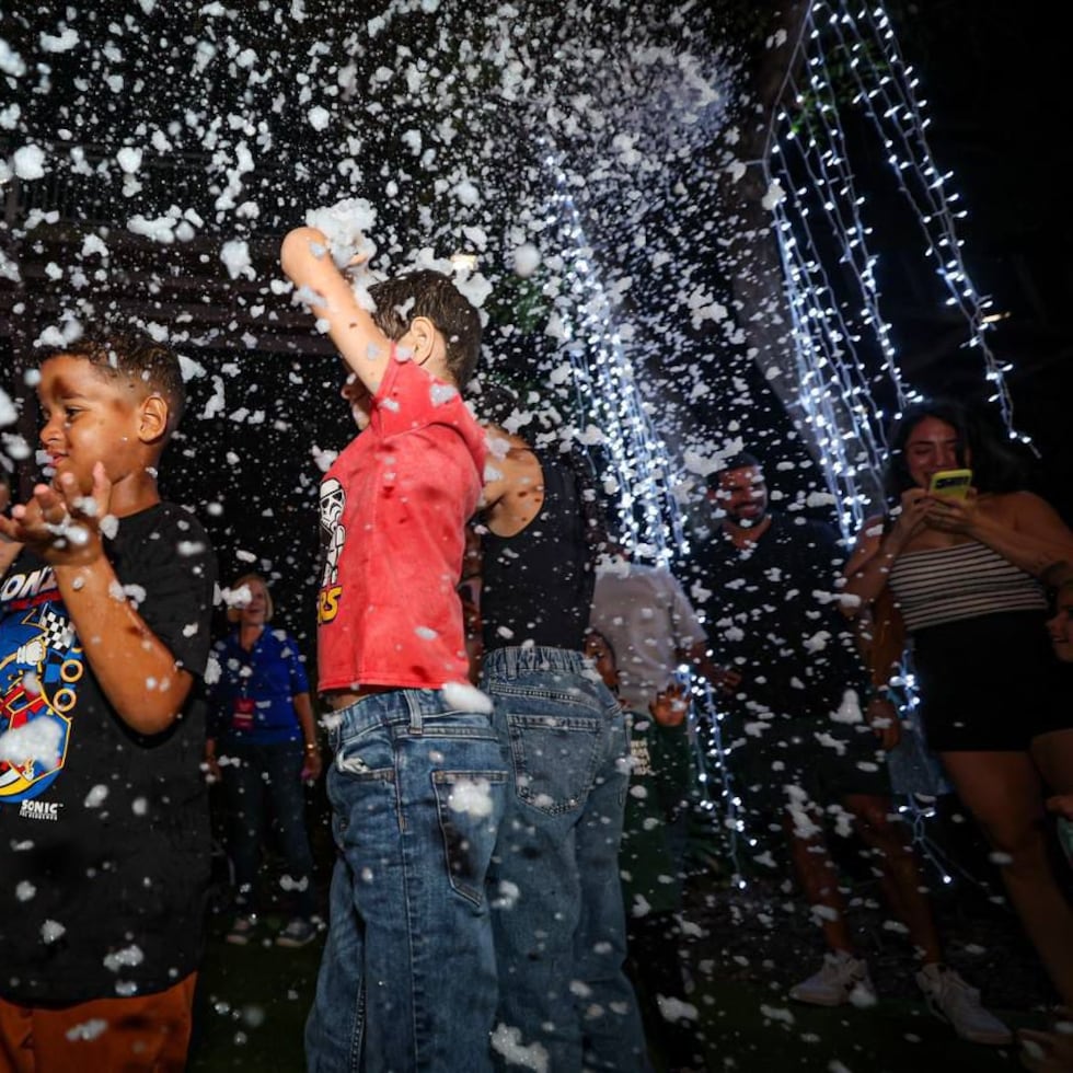Niños y adultos celebran entre luces y villancicos mientras una simulación de espuma crea el efecto de nieve.