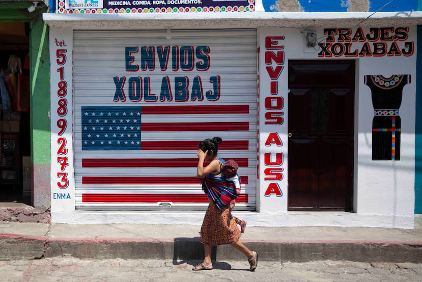 Una mujer camina con su hijo frente a un centro de remesas en Joyabaj, Guatemala. (AP Photo/Moises Castillo)