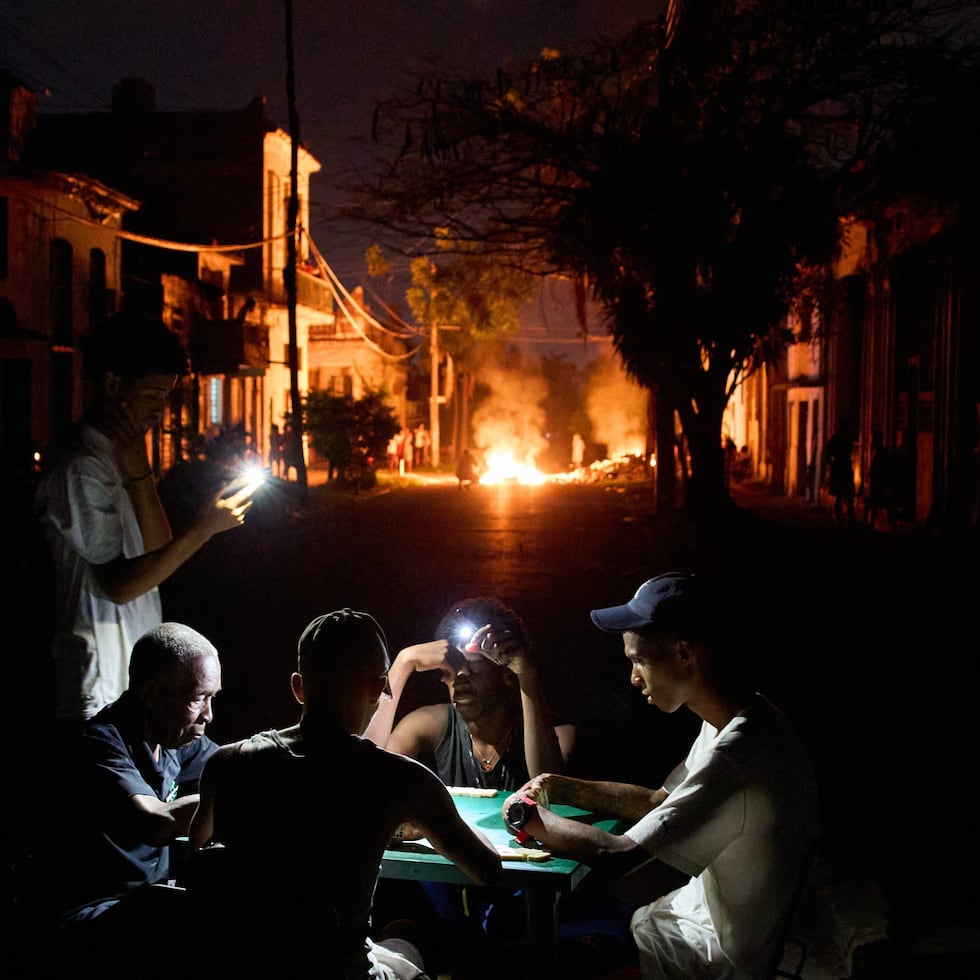 Varias personas se iluminan con sus teléfonos mientras juegan al dominó, al tiempo que arde en una calle de La Habana, Cuba, una hoguera provocada por los vecinos que protestaban contra los prolongados cortes de luz.