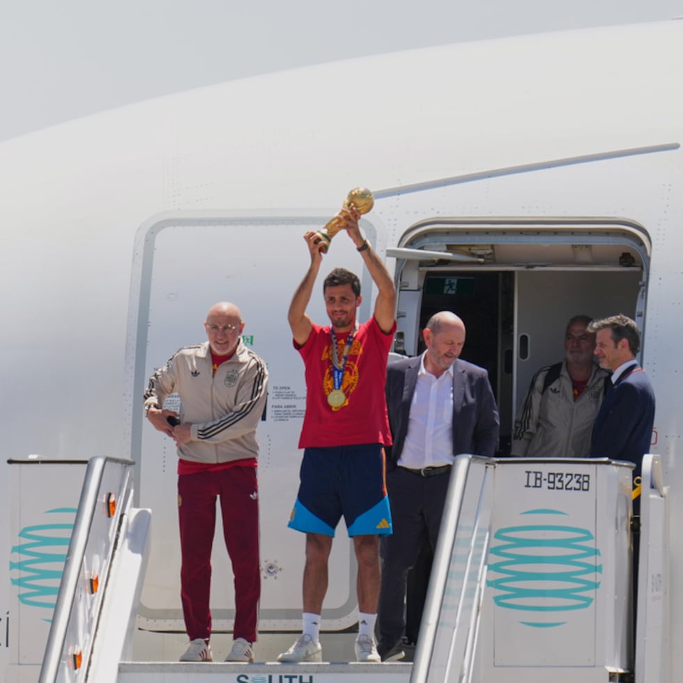 Rodrigo Hernández, de España, levanta el trofeo de la Copa del Mundo junto al seleccionador español Luis de la Fuente, a la izquierda, y el presidente de la Real Federación Española de Fútbol, Rafael Louzán, a su llegada al aeropuerto de Madrid.