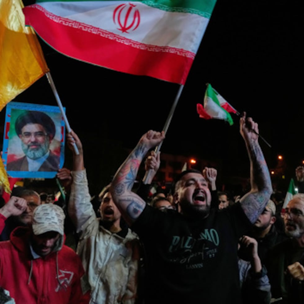 Manifestantes progubernamentales corean eslóganes mientras sostienen banderas iraníes.