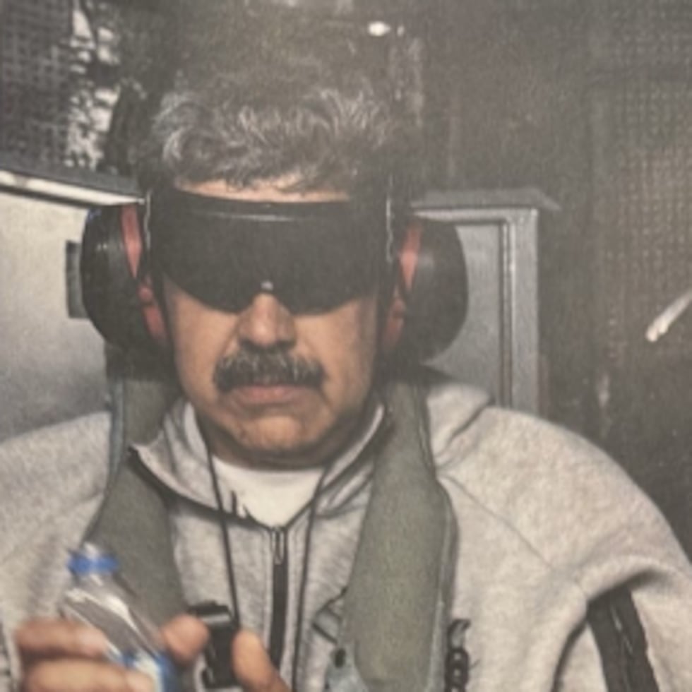 En la fotografía se ve al depuesto jefe del régimen con gafas oscuras para entorpecer la vista, auriculares para bloquear el sonido, salvavidas de flotación, una botella de agua y esposas en sus manos.