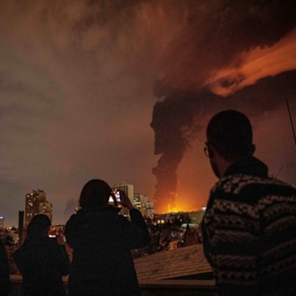 Residentes en Irán miran y toman fotos mientras las llamas y el humo se elevan desde una instalación de almacenamiento de petróleo atacada durante la campaña militar estadounidense-israelí en Teherán, Irán.