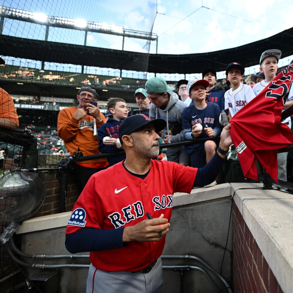 El ahora exmánager de los Red Sox de Boston, Alex Cora, en primer plano, firma autógrafos para los fanáticos antes de un partido contra los Orioles de Baltimore.