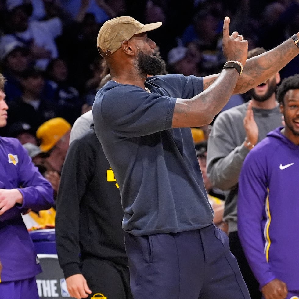 LeBron James, a la izquierda, celebra en la banca un canasto de los Lakers junto a su hijo Bronny James.