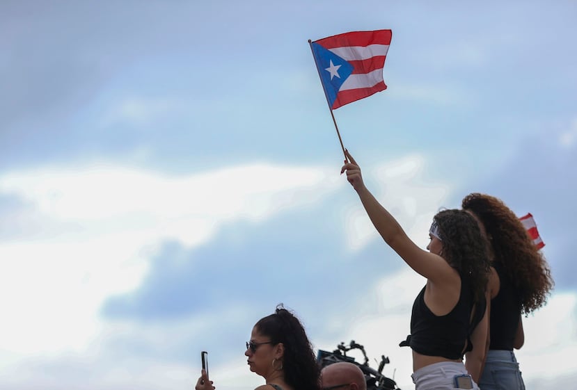 Una manifestante alza la bandera de Puerto Rico en el inicio de la marcha desde el Capitolio.