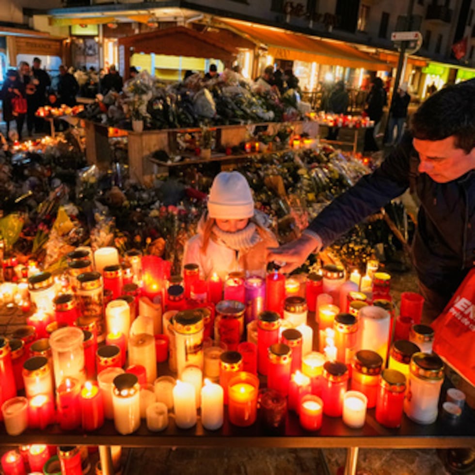 Un niño observa mientras un adulto coloca una vela fuera del bar sellado Le Constellation en Crans-Montana, Alpes suizos, Suiza, sábado 3 de enero de 2026, donde un devastador incendio dejó muertos y heridos durante las celebraciones de Año Nuevo.